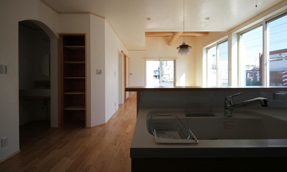 壁、天井共漆喰のナチュラルテイストの自然素材による木の家のキッチン（kitchin）からリビングを見る
